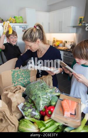 Woman and sons unloading fresh produce from box in kitchen Stock Photo