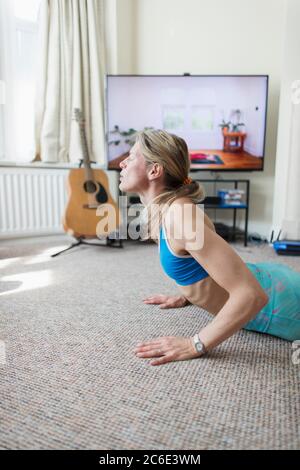 Woman practicing yoga at TV in living room Stock Photo