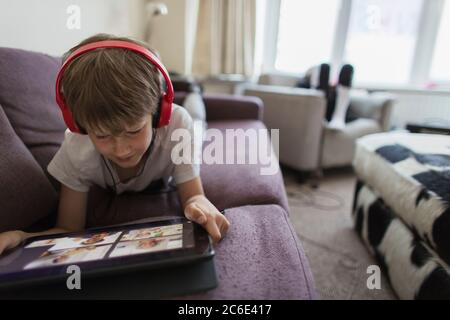 Boy with headphones and digital tablet homeschooling on sofa Stock Photo