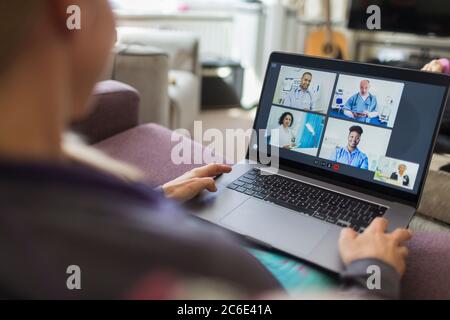 Woman with laptop video chatting with doctors from sofa Stock Photo