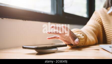 Woman Charging Smartphone Using Wireless Charging Pad At Home Stock Photo