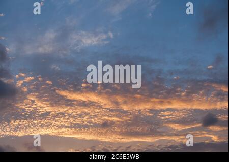 Setting or rising sun tinting Stratocumulus Cumulus as dramatic layers of clouds reflecting different sun rays due to altitude Stock Photo
