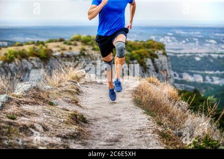 male runner in knee pads running on narrow mountain path