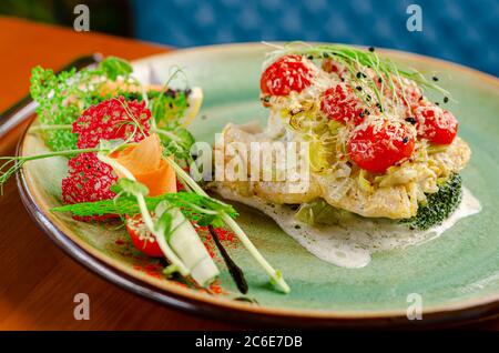 Cod fillet with tomatoes cherry and cheese, served with vegetables and micro greens. Close up Stock Photo