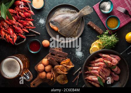 Grilled shrimps, crayfish, flatfish on a board and beer mug. Dark wooden table background. Stock Photo
