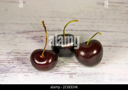 Three ripe sweet cherries with stems on a light wooden background Stock Photo