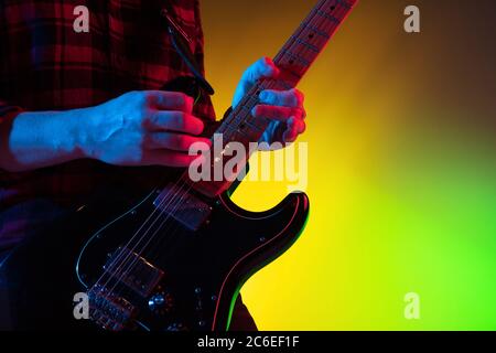 Close up young inspired and expressive musician, guitarist performing on gradient colored background in neon light. Concept of music, hobby, festival, art. Joyful artist, colorful, bright portrait. Stock Photo