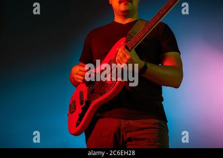 Close up. Young inspired and expressive musician, guitarist performing on gradient colored background in neon light. Concept of music, hobby, festival, art. Joyful artist, colorful, bright portrait. Stock Photo