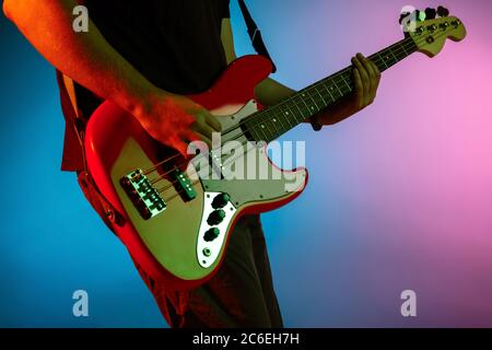 Close up. Young inspired and expressive musician, guitarist performing on gradient colored background in neon light. Concept of music, hobby, festival, art. Joyful artist, colorful, bright portrait. Stock Photo