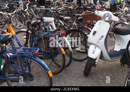 Amsterdam, Netherlands - February 24, 2017: White Vespa scooter stands near bicycles on a parking lot Stock Photo