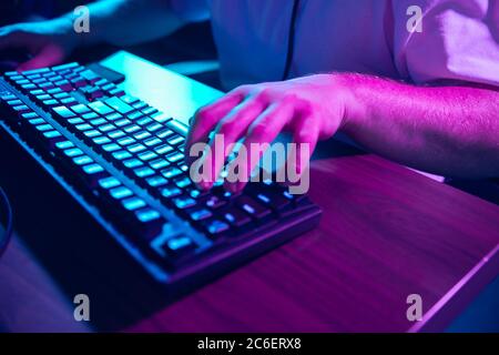 Cyber sport. Fully concentrated professional cybersport gamer playing important match. Caucasian male model practicing before tournament alone in neon light. E-sport, gamer, streamer. Close up. Stock Photo