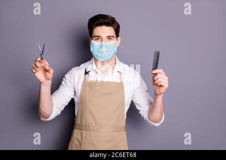 Portrait of his he attractive guy barber wearing safety mask holding in hands scissors comb social distance stop infection mers cov preventive Stock Photo