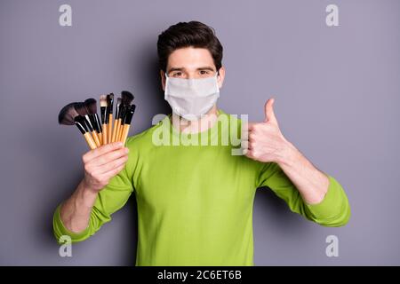 Portrait of his he attractive guy makeup artist wearing safety mask holding in hands many tassels mers cov influenza prevention showing thumbup Stock Photo