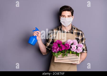 Portrait of his he nice guy gardener wearing safety mask holding in hands flowers pot watering plants stop infection mers cov disease isolated grey Stock Photo