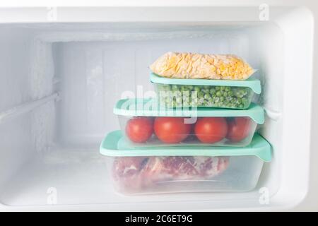 Frozen vegetables and meat in blue plastic containers. Frozen corn, peas, tomatoes, meat. Cold freezer. Empty space for text. Stock Photo