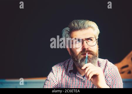 Portrait of thoughtful senior caucasian man with a grey beard and holding pen. Stock Photo