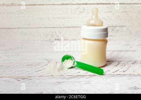 Baby bottle with milk formula on a white wooden background with empty place for text. Milk powder for the baby. Artificial nutrition of a newborn. Stock Photo