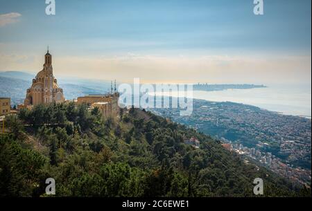 Our Lady of Lebanon Maronite church sits on a hill over the Jounieh bay, with Beirut capital city in the background, in Lebanon, Middle East Stock Photo