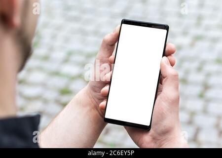 Image of mans hand holding modern black mobile phone with blank white screen. Man using mobile smart phone, close up. Stock Photo