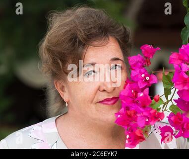 Close up portrait of beautiful older woman, smiling and standing whit a pink flowers. Stock Photo