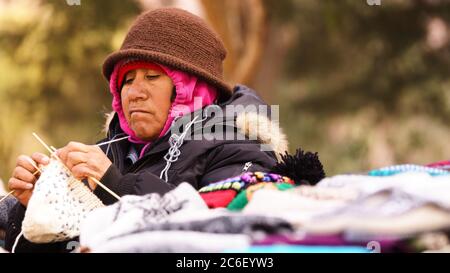 Native lady weaving surrounded by colorful clothing on the street Stock Photo