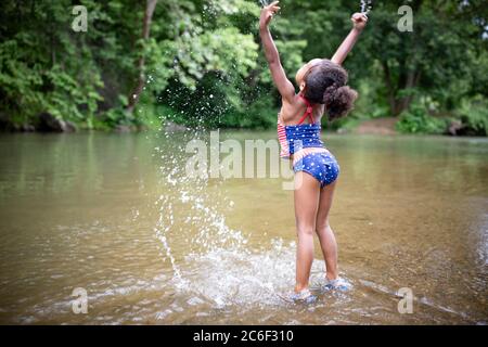 A young girl wades and splashes in the Shenandoah River, Virginia, USA.