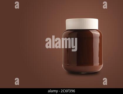 Chocolate spread or nougat cream with hazelnuts in glass jar on a brown background with space for text Stock Photo