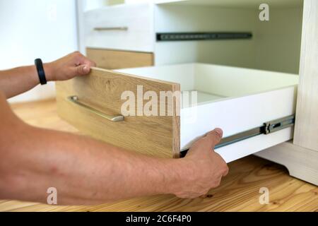 Close up of carpenter hands installing wooden drawer on sliding skids in contemporary cupboard cabinet. Stock Photo