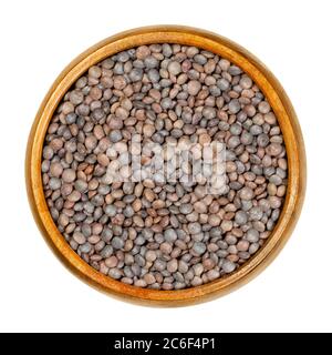 Unpeeled red lentils in wooden bowl. Dried seeds of Lens culinaris with their hulls, an edible legume, staple and a food crop. Closeup, from above. Stock Photo