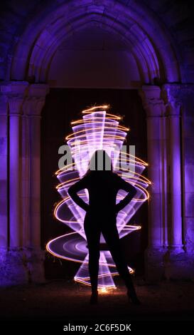 Silhouette of a woman in lightpainting session. Gothic style sculpture with arch. Curved abstract shape with bengal fire. Stock Photo