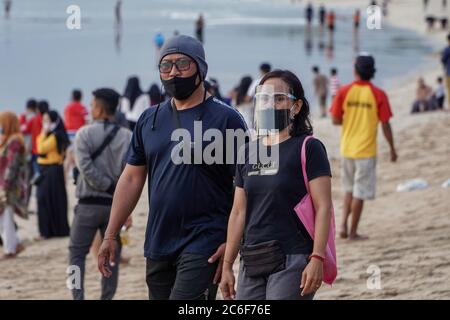 Badung, Bali, Indonesia. 9th July, 2020. A woman wears a faceshield while walk along the beach. Local government start to reopen famous tourism icon of Kuta Beach for Bali citizens as a stage of ''new normal'' plan. Kuta Beach has been closed since March 30, 2020 due to Covid-19 coronavirus concern. Credit: Dicky Bisinglasi/ZUMA Wire/Alamy Live News Stock Photo