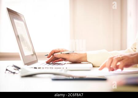 Close-up shot of businesswoman’s hand typing on laptop and using calculator while working at office desk. Home office. Stock Photo