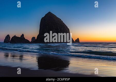 Birds fly above Haystack Rock and sea stacks at sunset along Cannon Beach in Oregon Stock Photo