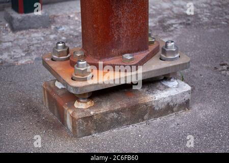 Anchoring of a rusty iron pillar to old concrete foundation with huge steel nuts and bolts. Close up image. Stock Photo