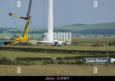 Larkhall, Scotland, UK. 9th July, 2020. Pictured: A huge wind turbine stands a few hundred feet tall whilst its blades lay on the ground ready to be attached. Green energy is is big business, and if the UK is to archive its targets for renewable energy then more wind turbines onshore and offshore need to be built. Credit: Colin Fisher/Alamy Live News
