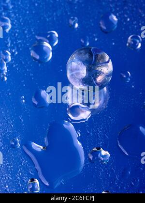 Blue accent colour, single glass marble and water droplets on blue, Stock Photo