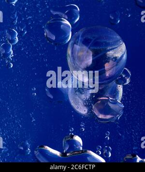 Blue accent colour, single glass marble and water droplets on blue, Stock Photo