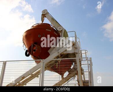 Bright orange decommissioned capsule life boat suspended in a white launch frame next to the bay in Santander Cantabria Spain Stock Photo