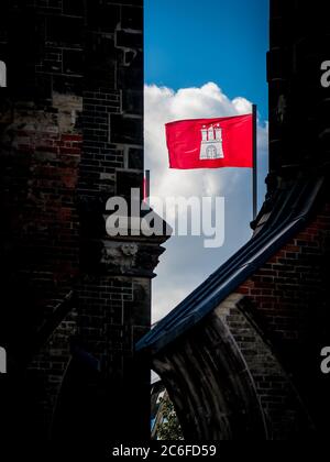 red flag of hanseatic city of hamburg with coat of arms is waving in the wind on top of the st. nikolai memorial Stock Photo