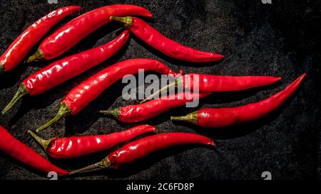 top view of a group of red chili peppers placed in a flame shape side by side on a cast iron surface with copy space on the right side, symbol picture Stock Photo