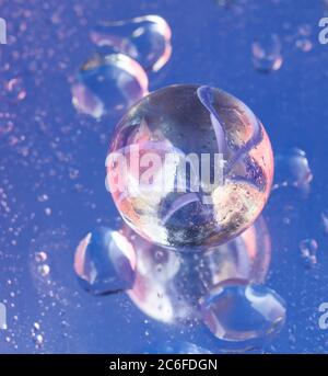 Blue accent colour, single glass marble and water droplets on blue, Stock Photo