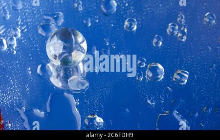 Blue accent colour, single glass marble and water droplets on blue, Stock Photo