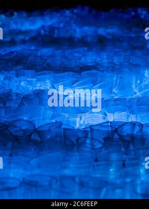 huge heap of thrown away used transparent disposable plastic cups illuminated by blue light, environmental pollution Stock Photo