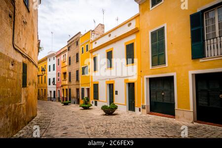 quaint narrow alley with colorful painted houses in the old town of ciutadella with vanishing point to the left side Stock Photo