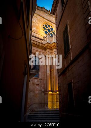 upright view of neoclassical gothic ciutadella de menorca cathedral from a narrow alley in the old town illuminated in the twilight, minorca Stock Photo