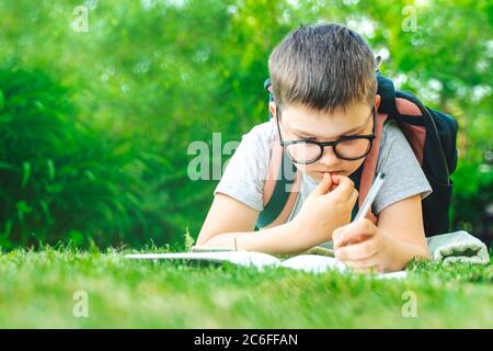 Back to school. schoolboy toddler laying on grass writing in exercise book making homework. male kid drawing writing math outdoors. school education Stock Photo