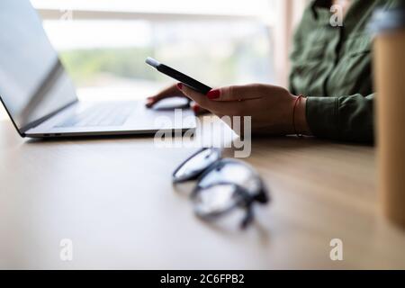 Businesswoman working at office desk and texting with her mobile phone Stock Photo