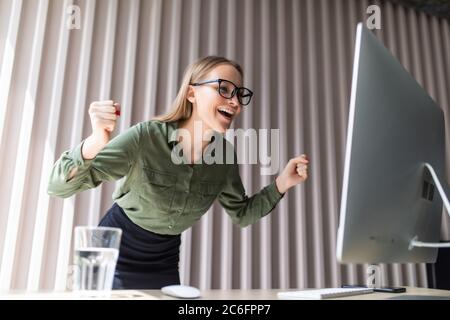 Excited executive wearing suit raising arms watching a desktop monitor at office Stock Photo