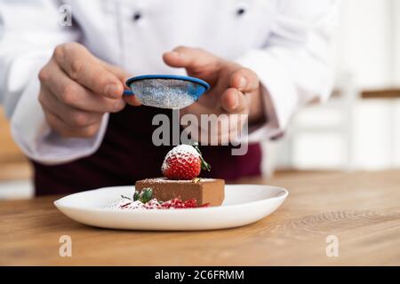 Close up pastry chef decoration delicious dessert dish, serving for customers in bakery, garnishing dessert plate in commercial kitchen. Stock Photo