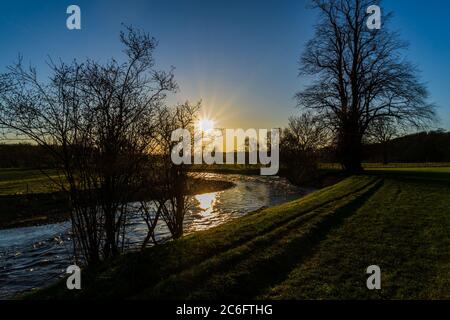 The sun setting behind a tree reflecting on the river Eamont penrith Stock Photo